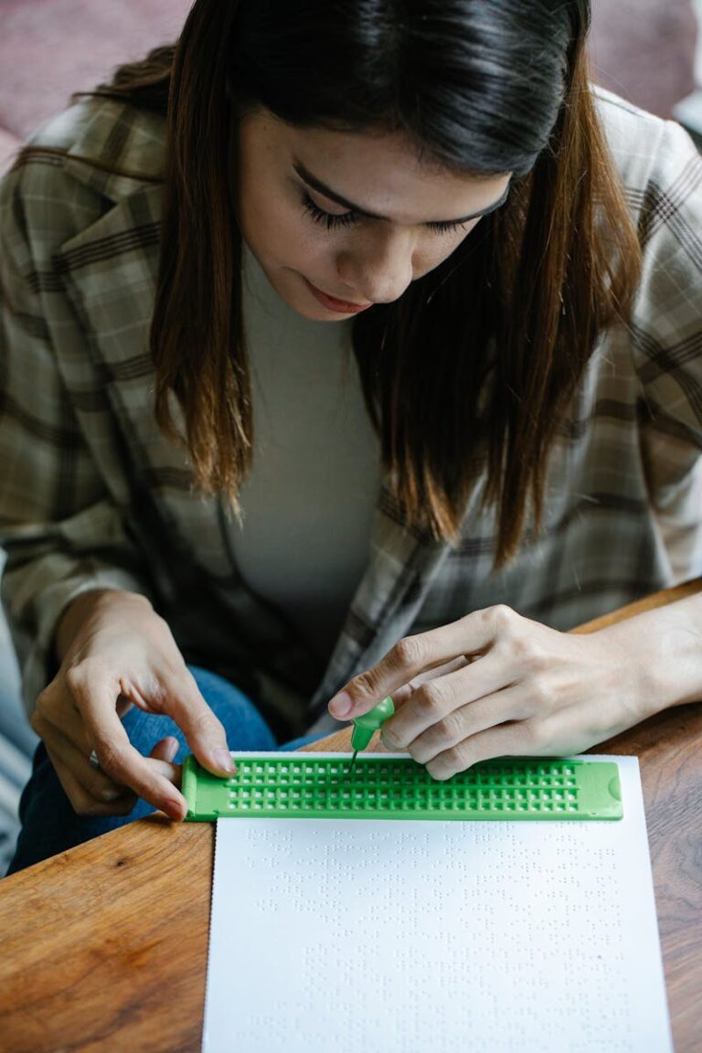 Focused woman using a braille slate and stylus to write on paper indoors.